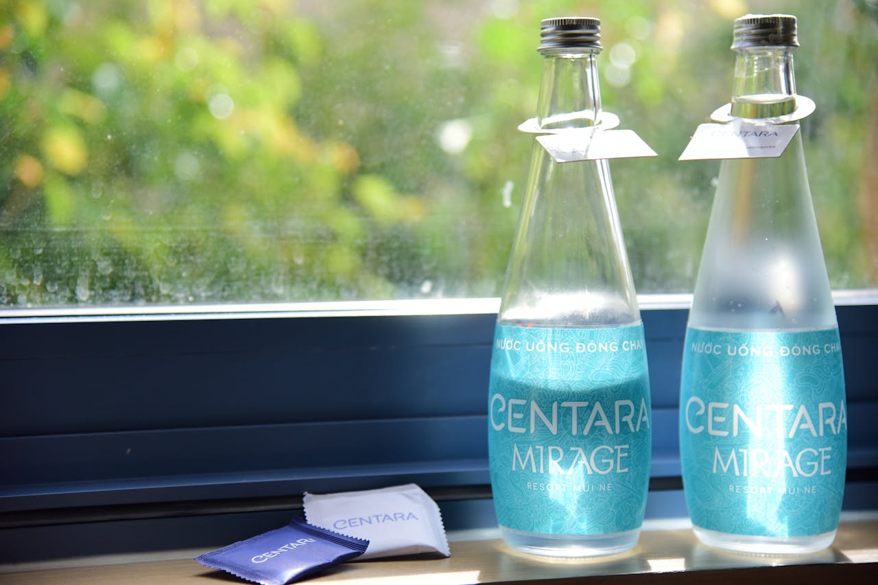 Two Centara Mirage water bottles by a sunlit window with vibrant greenery outside.