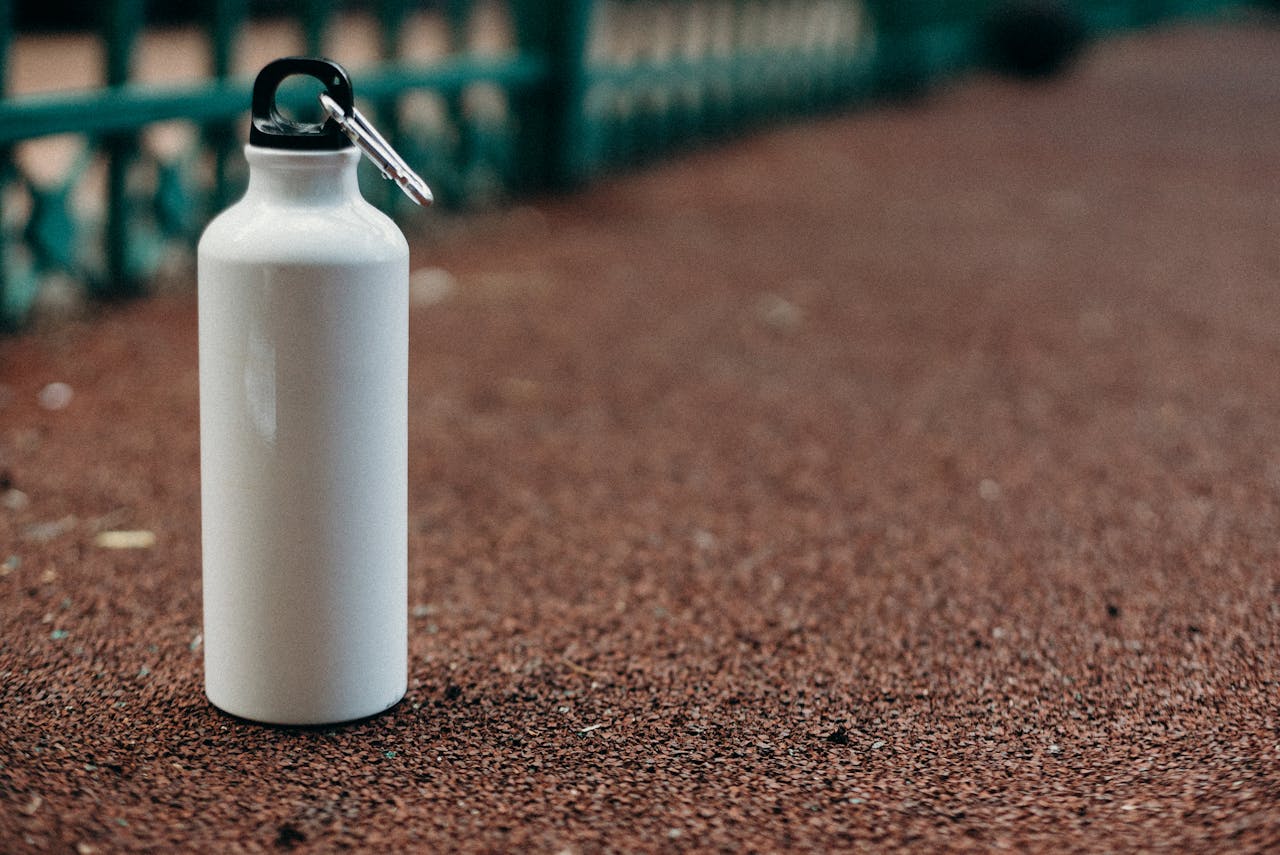 Close-up of a white water bottle with carabiner on an outdoor track.
