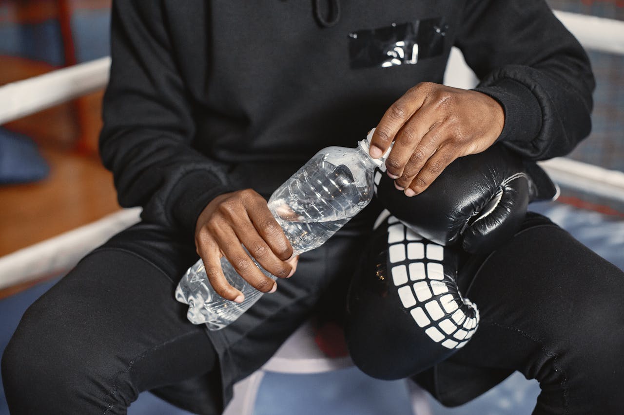 A boxer in black outfit holding a water bottle during a break indoors.